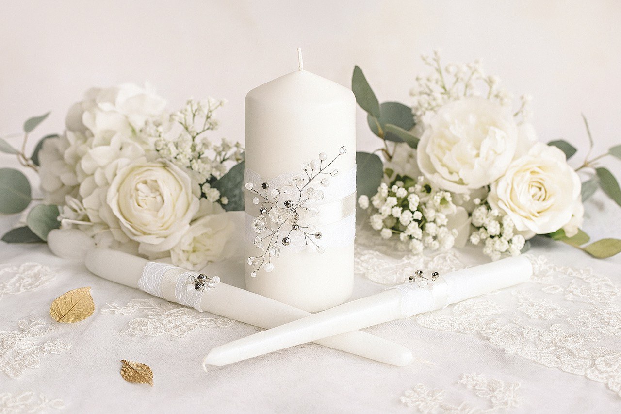 White candle with decorative elements surrounded by white flowers on a light background
